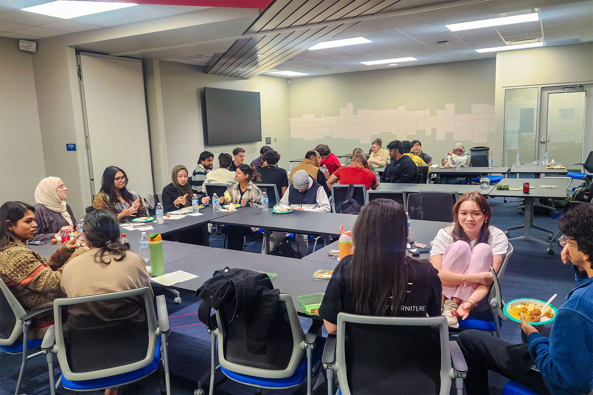 students sitting at tables talking and eating food at gathering