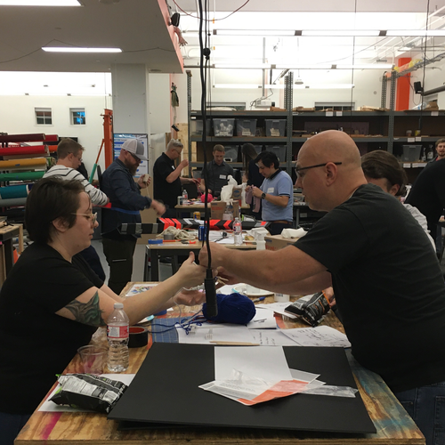A group of people sitting around a table in a workshop, engaged in a hands-on activity.