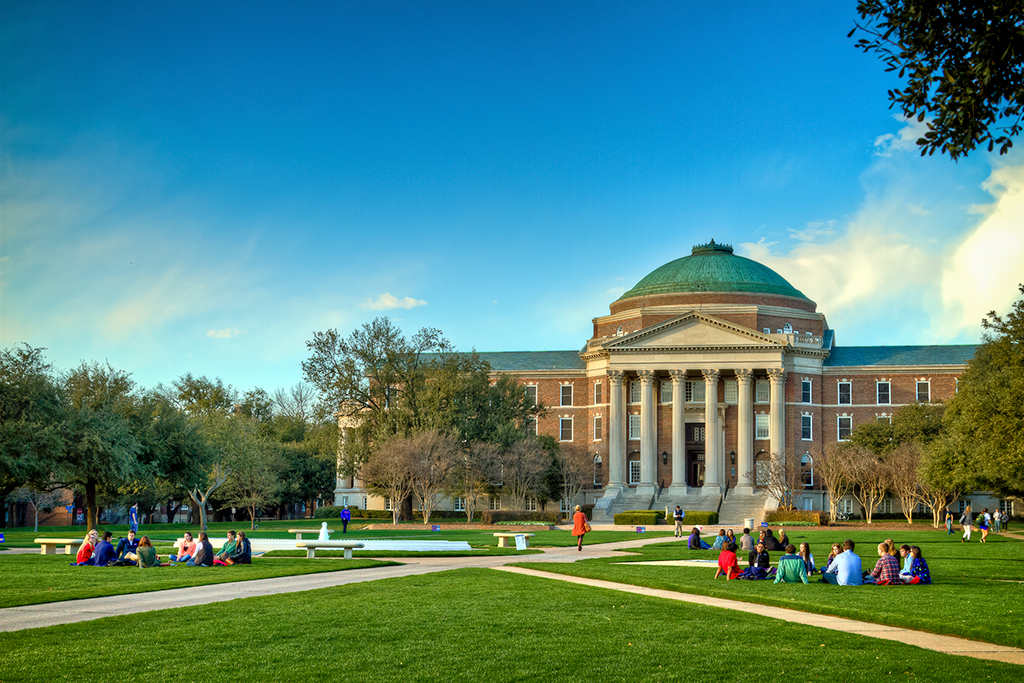 People seated on the front lawn of Dallas Hall. 