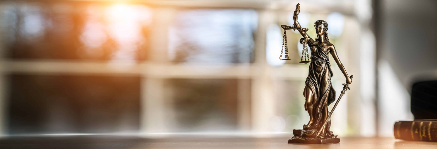 Pre-Law Image Header Blind Justice figurine on a wooden desk with a window view.