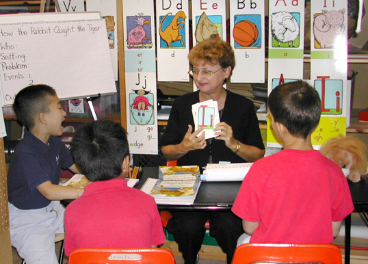 A teacher at a table, instructing students in letter recognition as part of an early reading intervention program.