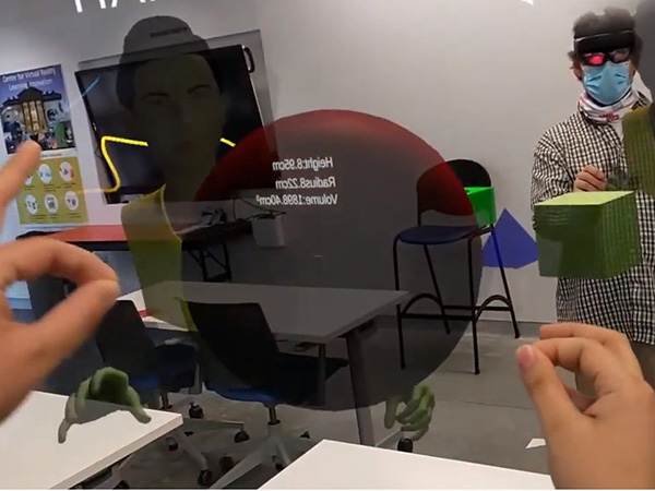 Augmented Reality view of participants interacting with 3D shapes for middle-school educational purposes.  