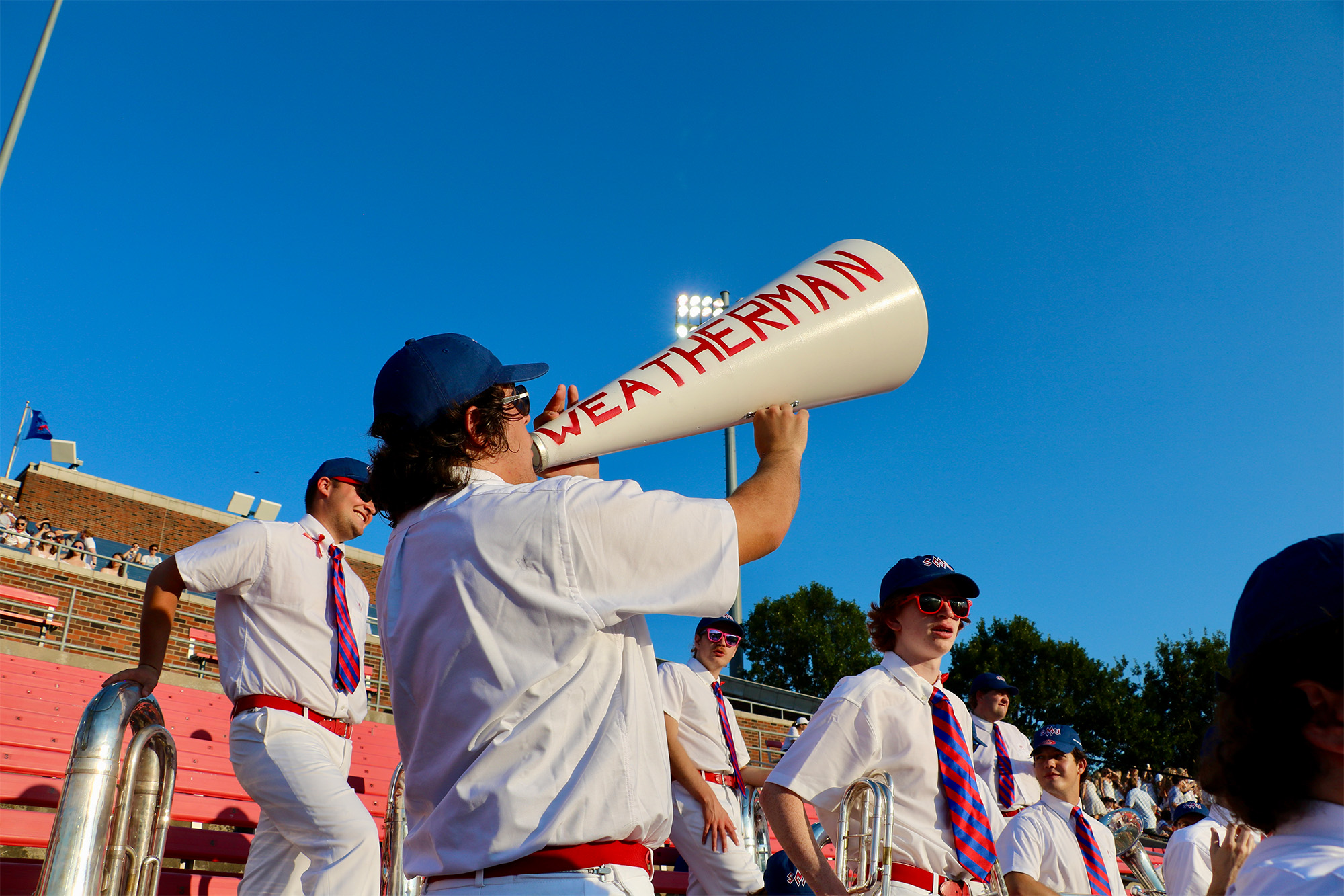 Mustang Band member shouting through "Weatherman" megaphones outside in stands at a football game